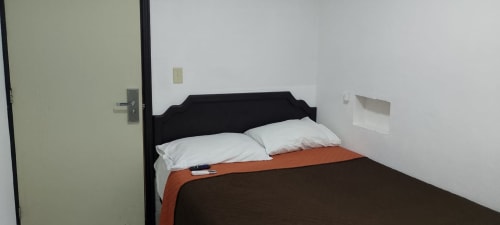 Habitación del Hotel Estrella en Matamoros con cabecero negro, almohadas blancas y ropa de cama naranja