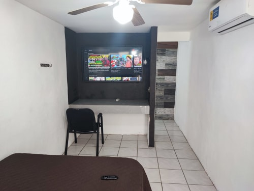 Habitación de huéspedes del Hotel Estrella en Matamoros con TV de pared, silla negra y pisos de azulejo