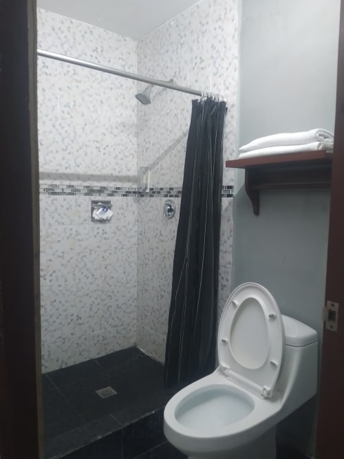Baño moderno del Hotel Estrella en Matamoros con inodoro blanco, ducha con azulejos negros y mampara de vidrio, y baldosas blancas