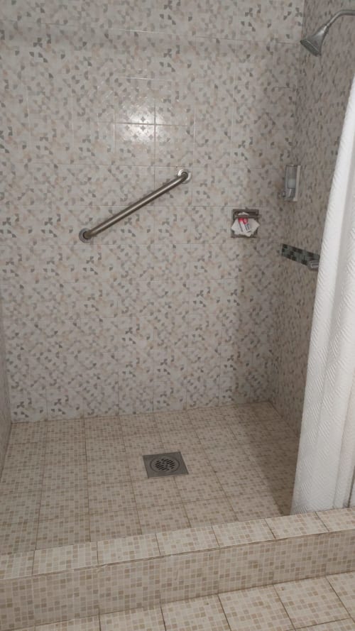 Ducha de acceso directo del Hotel Estrella con azulejos beige, barra de seguridad y desagüe en Matamoros