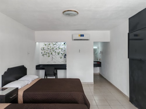 Habitación del Hotel Estrella en Matamoros con cama, escritorio con mural de árbol, aire acondicionado y entrada al baño