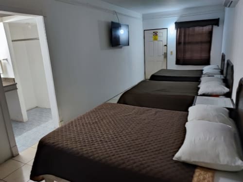 Habitación del Hotel Estrella en Matamoros con múltiples camas, baño, TV y ventana con cortinas marrones