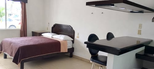 Habitación del Hotel Estrella en Matamoros con cama de manta borgoña, mesa de comedor con sillas negras, cocineta y