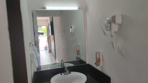 Baño del Hotel Estrella en Matamoros con lavamanos, espejo, secador de cabello montado en pared y dispensador de artículos de aseo