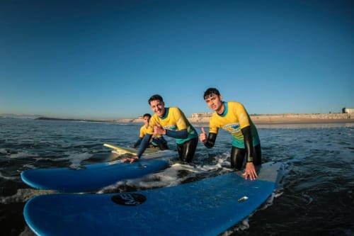 Surfing lesson at Vila Alexandra hostel in Costa da Caparica, Portugal with instructors and guests in yellow wetsuits