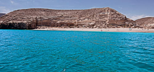Aguas turquesas del Mediterráneo y playa de arena cerca de Carboneras con acantilados rocosos, perfecta para los huéspedes del Hostal Juan Carlos