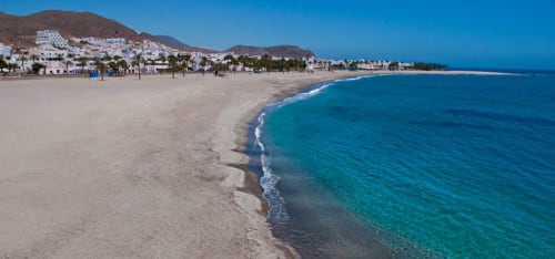 Playa de Carboneras con aguas turquesas, arena blanca y pueblo encalado rodeado de colinas desérticas bajo cielo azul