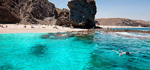 Aguas turquesas y acantilados rocosos en la playa de Carboneras cerca del Hostal Juan Carlos, España