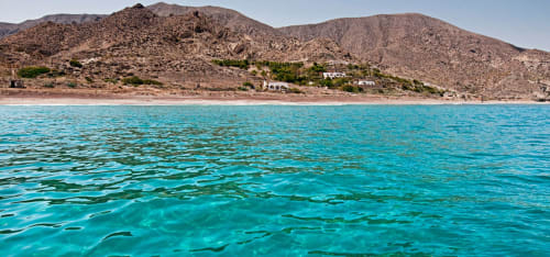 Aguas turquesas del Mediterráneo con montañas áridas y Hostal Juan Carlos en Carboneras, España