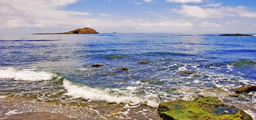 Costa rocosa con olas en el Hostal Juan Carlos de Carboneras, España, con una pequeña isla y aguas azules del Mediterráneo