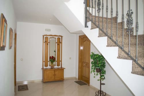Luminoso recibidor del Hostal Juan Carlos en Carboneras con muebles de madera, escalera con barandillas ornamentales y plantas en macetas