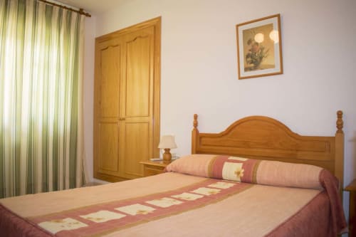 Habitación del Hostal Juan Carlos en Carboneras con cama de madera, cortinas verdes y armario de madera