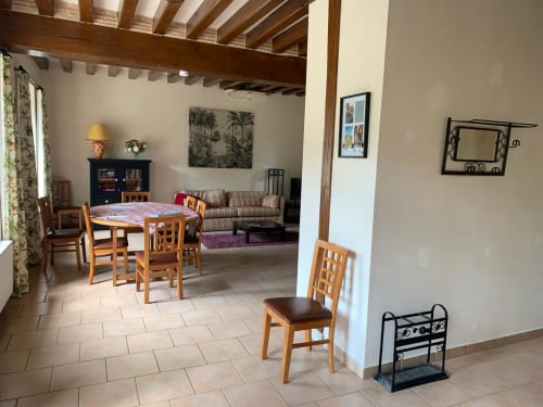 Salle à manger du gîte Accolade à Châteaudun : poutres en bois, table, canapé rayé et vue sur le jardin