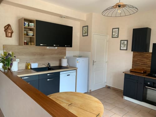 Cuisine de cottage moderne à Accolade Châteaudun avec mobilier noir, plans de travail en bois et coin repas vue sur jardin.