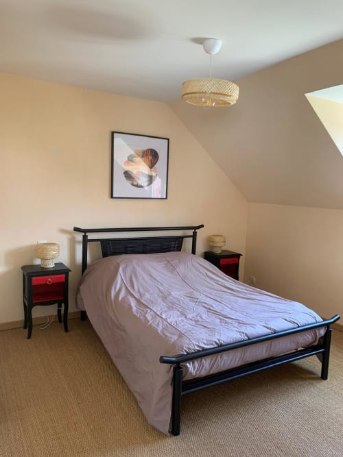 Chambre accueillante du gîte Accolade à Châteaudun avec lit en métal noir, luminaire suspendu tressé et vue sur le jardin