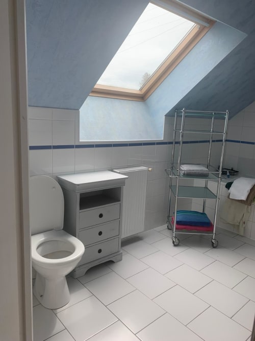 Salle de bains lumineuse du gîte Accolade à Châteaudun avec puits de lumière, carrelage blanc, toilettes, lavabo et rangements