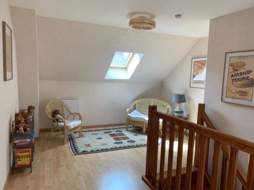 Chambre mansardée lumineuse au cottage Accolade à Châteaudun avec fenêtres de toit, balustrade en bois, chaises en rotin et ambiance ludique