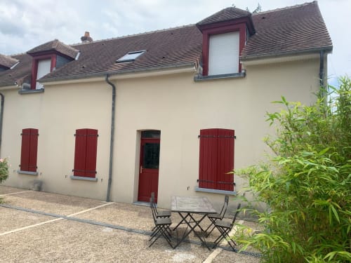 Cottage Accolade à Châteaudun, façade crème, volets rouges, jardin avec salon de jardin