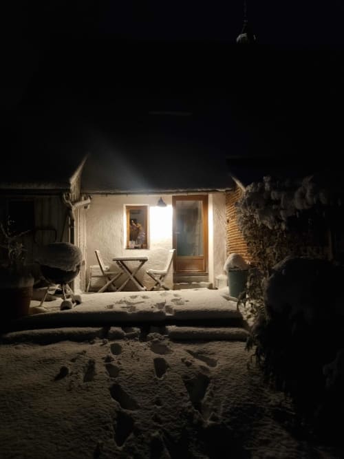 Le gîte La Dragonne en bord de mer la nuit à Bellême, avec sa terrasse de sable et ses fenêtres illuminées