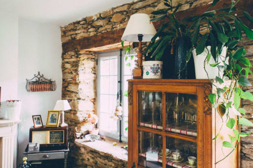 Intérieur rustique de la Casa Rural La Perla avec murs en pierre apparente, meuble en bois, plantes en pot et lampe blanche