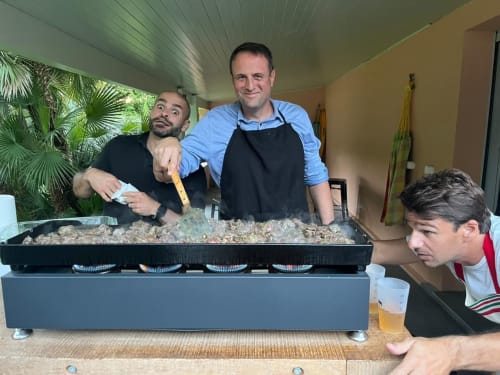 Staff members preparing paella at La Conciergerie Biarritz, a French bed and breakfast, during a cooking experience.