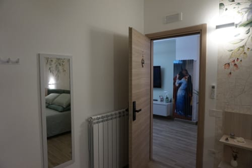Ingresso della suite La Dimora Di Ipno con moderne porte in legno, termosifone e vista della camera da letto con arredamento botanico