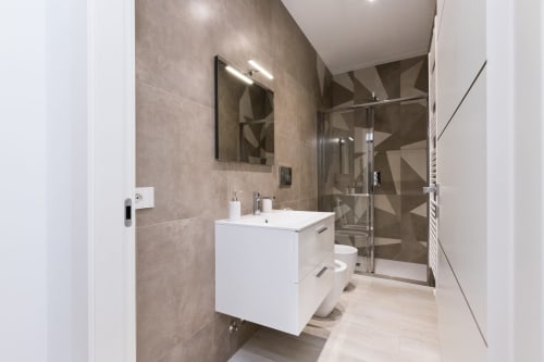 Modernes Badezimmer in Magnolia Apartments Milan mit weißem Waschbecken, Spiegel, geometrischen Wandfliesen und verglaster Duschkabine