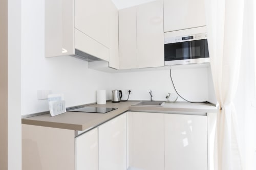 Moderne weiße Küche in Magnolia Apartments Mailand mit Edelstahlarbeitsplatten, Einbauofen und Geräten