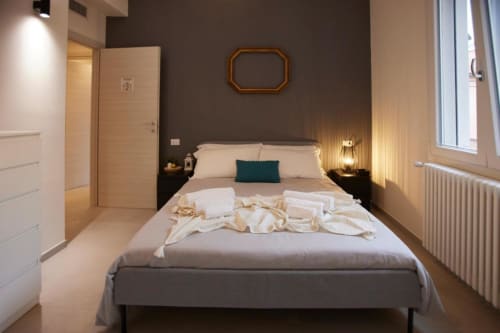 Camera moderna con pareti grigie, letto matrimoniale, biancheria bianca e illuminazione calda presso l'hotel L.H.A. a Ferrara, Italia