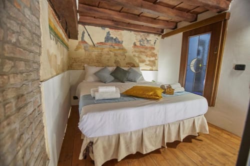 Cozy hotel bedroom in Ferrara with exposed brick, wooden beams, white bedding, and vintage wall mural