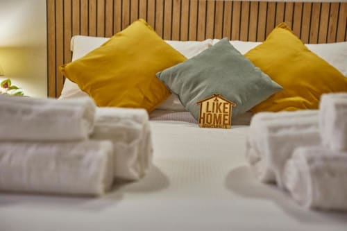 Moderno letto d'hotel con cuscini gialli e grigi, asciugamani bianchi e logo Like Home Apartments nella proprietà L.H.A. a Ferrara