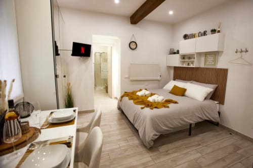 Modern studio bedroom in Ferrara hotel with bed, kitchenette, wall-mounted TV, and warm lighting