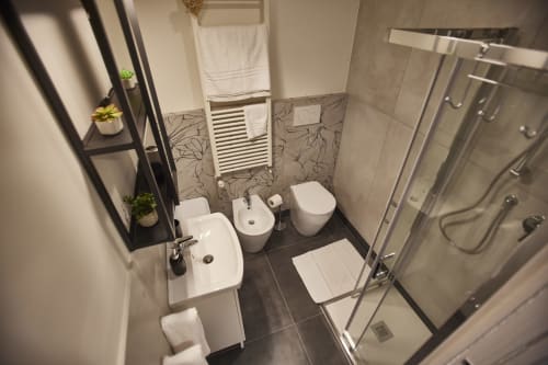 Modern bathroom in LikeHome San Romano cottage, Ferrara, with white fixtures, dark tiled floor, and glass shower enclosure