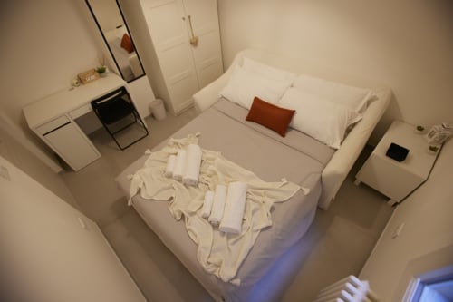Modern bedroom in LikeHome San Romano cottage, Ferrara, with white bed, cream linens, rust pillow, desk, and city views