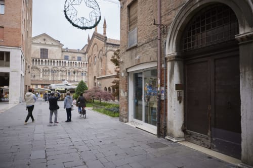Medieval piazza in Ferrara, Italy with historic brick buildings, decorative wreath, and pedestrians on stone plaza