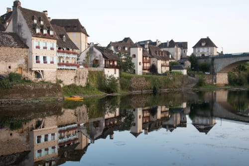 Village médiéval au bord de la rivière avec bâtiments en pierre et pont se reflétant dans l'eau calme, Darazac France