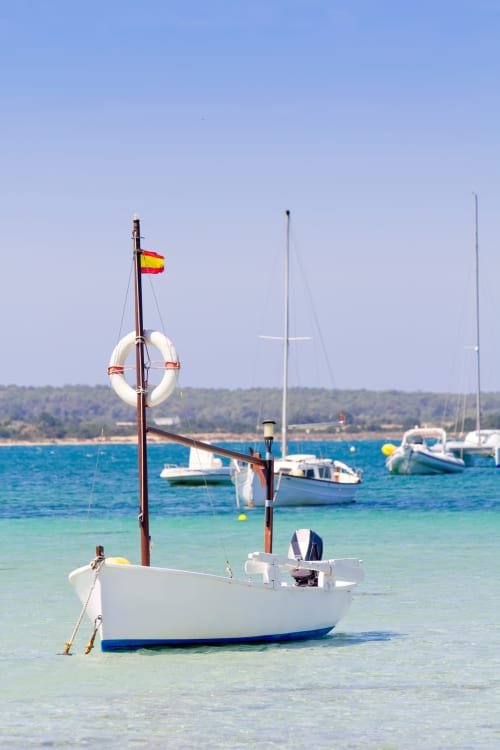 Barco de pesca blanco con bandera española fondeado en aguas turquesas frente a La Savina, Formentera