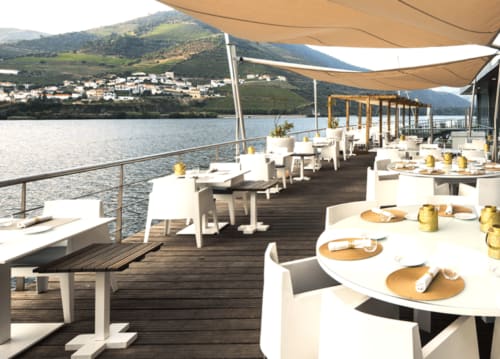 Quinta Do Fraguil's waterfront dining terrace overlooking Douro river with white chairs, tables, and tan shade sails