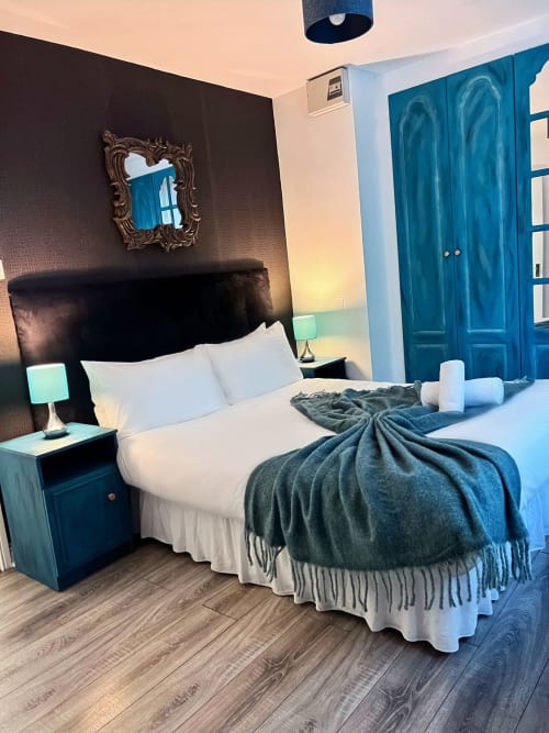 Stylish Dublin apartment bedroom with black headboard, white linens, teal accents, ornate mirror, and hardwood floors