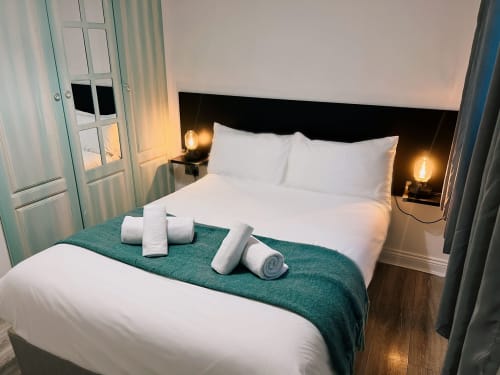 Modern bedroom at Dublin Exchange Suites with white linens, rolled towels on teal runner, ambient lighting, and hardwood