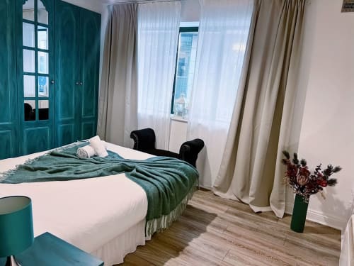 Modern bedroom at Dublin Exchange Suites with teal doors, white bed, green throw blanket, and city view windows