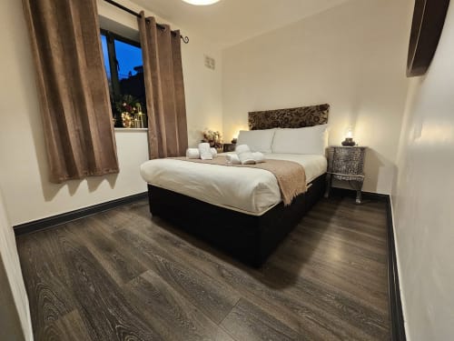 Modern bedroom at Dublin Exchange Suites with queen bed, white linens, dark wood floors, window with curtains, and bedside