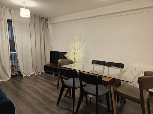 Modern dining area in Dublin Exchange Suites apartment with glass table, black chairs, illuminated tree decoration, and TV in