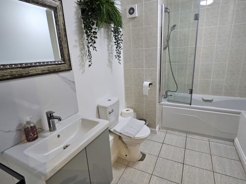 Modern bathroom in Dublin Exchange Suites apartment with sink, toilet, bathtub, shower enclosure, and hanging plant decor