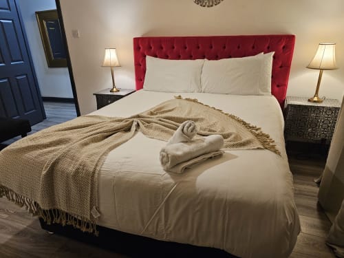 Modern bedroom at Dublin Exchange Suites with red tufted headboard, cream bedding, beige throw, and bedside lamps