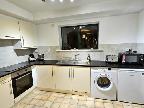 Modern kitchen in Dublin Exchange Suites family apartment with white cabinets, black counters, washing machine, sink and