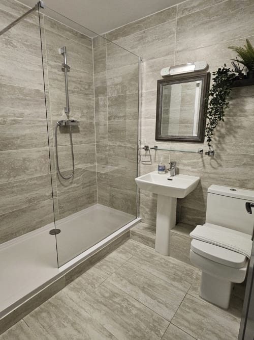 Modern bathroom in Dublin Exchange Suites with walk-in shower, pedestal sink, toilet, and gray tile throughout