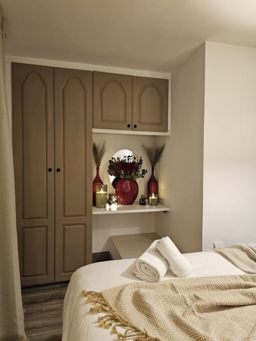 Bedroom in Dublin Exchange Suites with made bed, wardrobe, shelf with decorative red vase and flowers, candles