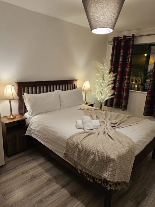 The Liffey Suite bedroom at Dublin Exchange Suites with wood bed, white linens, side lamps, and burgundy curtains