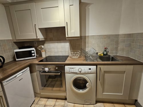 Modern kitchen in The Liffey Suite at Dublin Exchange Suites with white cabinets, wood counters, washing machine, oven, and